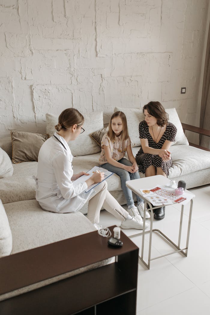 A doctor consults a mother and daughter in a comfortable indoor setting.
